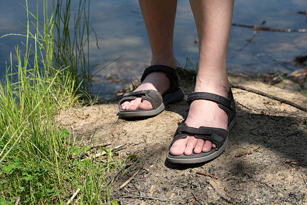 istock Bare feet in sandals resting on sandy ground beside a tranquil lake. Lush greenery frames this peaceful summer setting under a clear blue sky 2218950365
