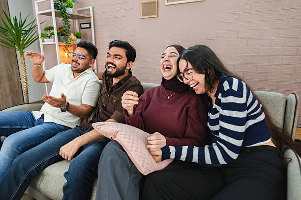 istock Four friends laughing and having fun watching tv on sofa at home 2218959700