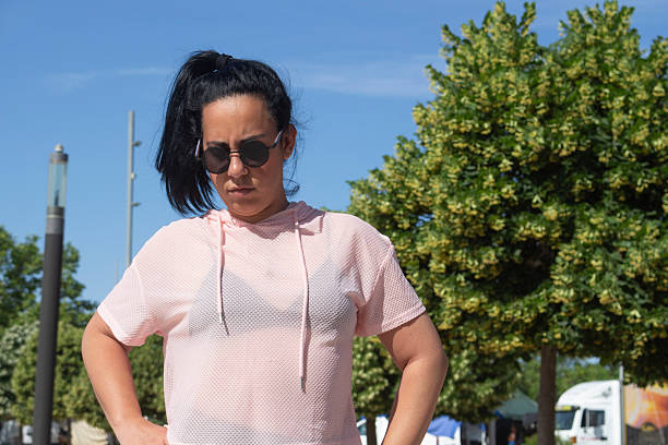 Confident sportswoman standing with hands on her hips, looking down, in a park during a sunny day