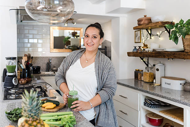 Latin young woman overweight preparing detox or green juice in kitchen at home in Mexico Latin America, Mexican female plus size preparing vegetables for diet stock photo