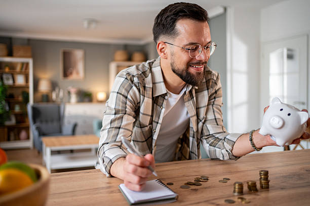 istock Young man saving money at home using piggy bank and notebook 2218966781
