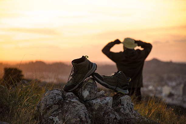 istock Trekking boots on rocks with a man on the mountain as dusk falls. 2218967048