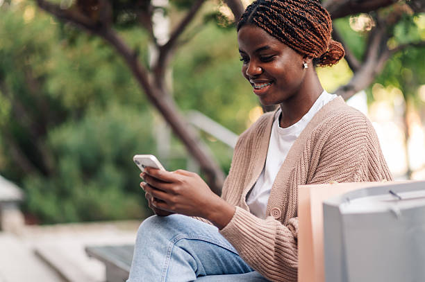 istock Young woman using smartphone while sitting on bench after shopping 2218967141