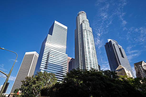 Low-angle view of modern skyscrapers under a bright blue sky in downtown Los Angeles. The image captures the city's iconic mix of contemporary architecture and Californian natural elements, symbolizing growth, finance, and West Coast lifestyle.