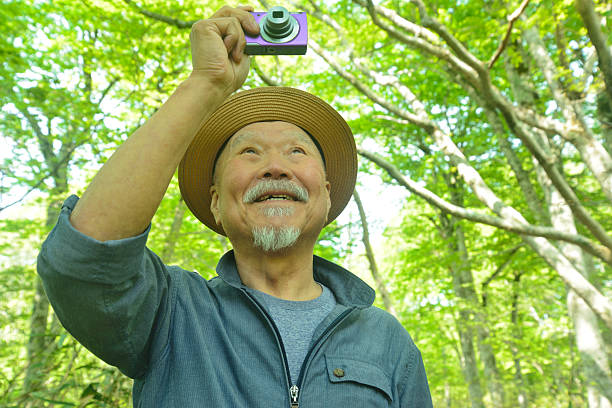 istock Smiling old man taking pictures of a beech forest with a digital camera 2218969423