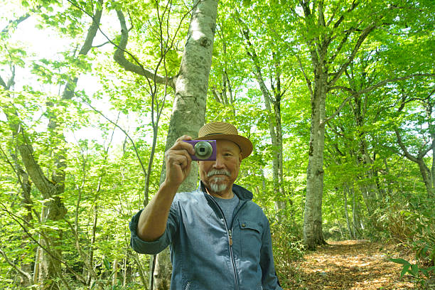 istock Smiling old man taking pictures of a beech forest with a digital camera 2218969426