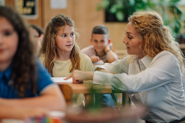 istock Teacher helping young girl student in elementary school classroom 2218971153