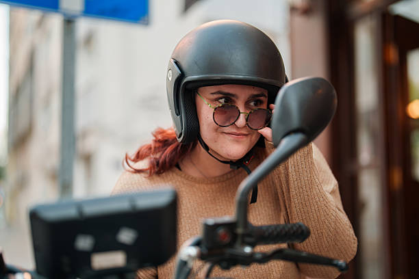 A young woman is seen riding her scooter and putting on her helmet.