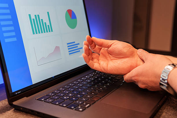istock Businessman experiencing wrist pain while working on laptop with charts on screen 2218983525