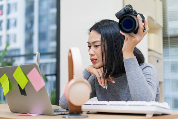istock Creative Asian woman working on laptop in modern office while holding a camera and focusing on her project 2218991019