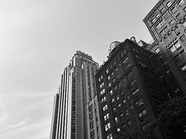 A low-angle black-and-white photo captures historic and modern buildings rising sharply into the sky in Manhattan.