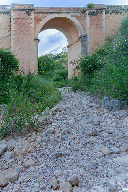 ronda,malaga,spain Dry riverbed with rocks and vegetation passing under an old brick bridge with a large arch
