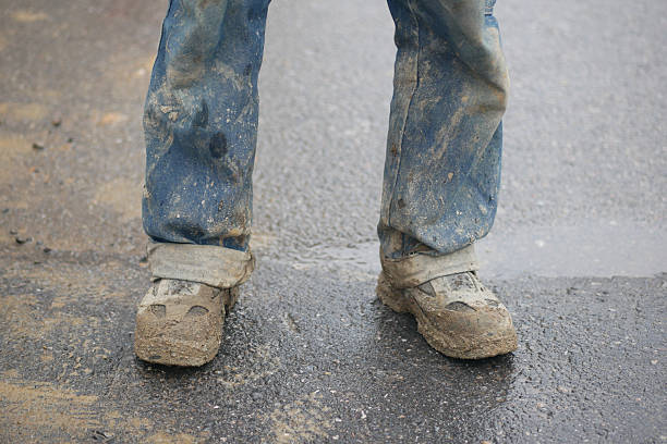 Construction worker with dirty shoes stands on a wet surface.
