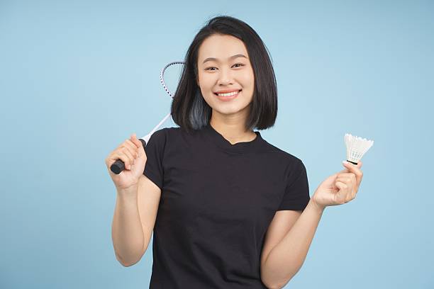 Young Asian woman smiling while holding a badminton racket and shuttlecock against a blue background