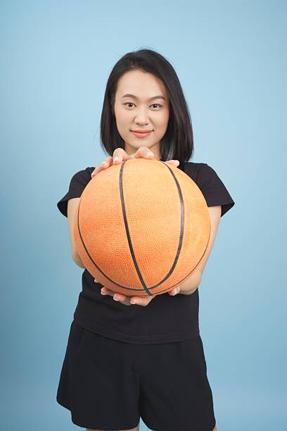 istock Young woman holds basketball in a studio with blue background while posing confidently 2219006400