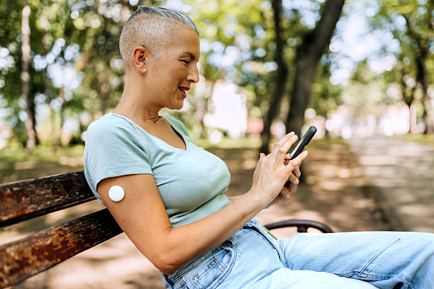 istock Woman with glucose sensor attached on her arm using smart phone at public park 2219010072