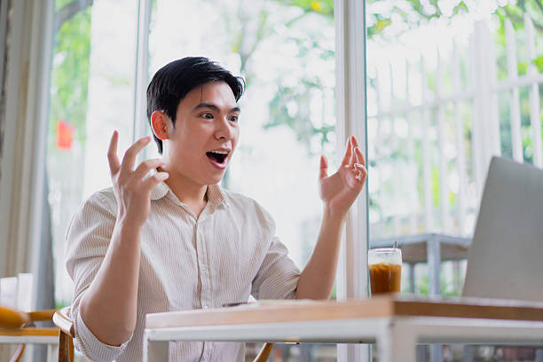 istock Young man expresses excitement while video chatting in a modern cafe during the afternoon 2219011850