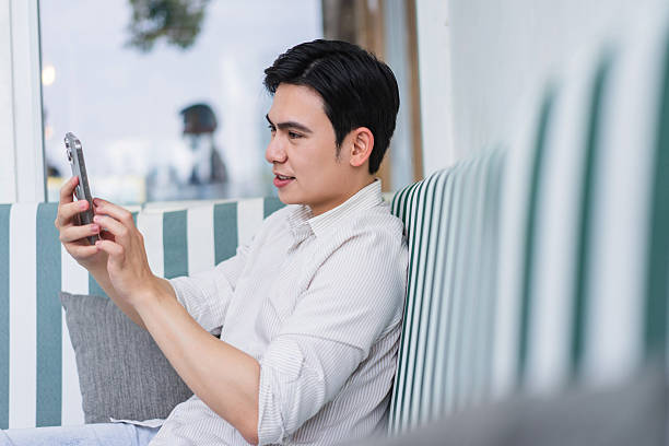 istock Young Asian man using smartphone while relaxing in a cozy indoor cafe seating area during the afternoon 2219011863