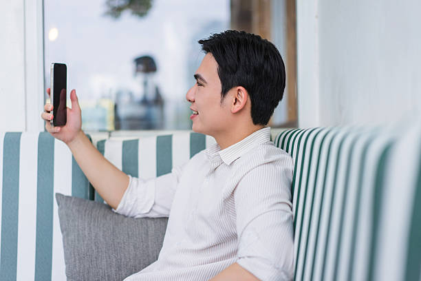 Young Asian man enjoying a video call while relaxing in a modern cafe setting during the afternoon