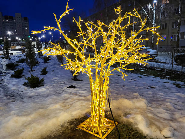 There is a glowing artificial tree on the street, a beautifully decorated and illuminated pedestrian street. The bokeh effect of blurred garlands on the background of the night sky