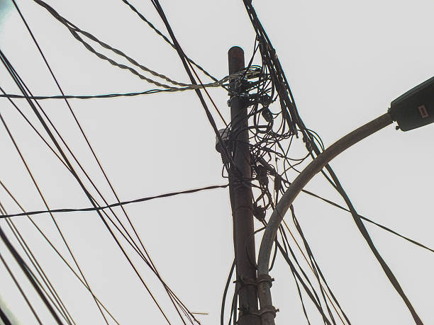 istock A utility pole with tangled wires and a streetlight against a bright sky. 2219013548