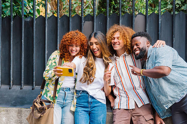 istock Diverse group of young friends taking group selfie, laughing and making playful hand gestures while standing together on urban street, expressing camaraderie 2219015225