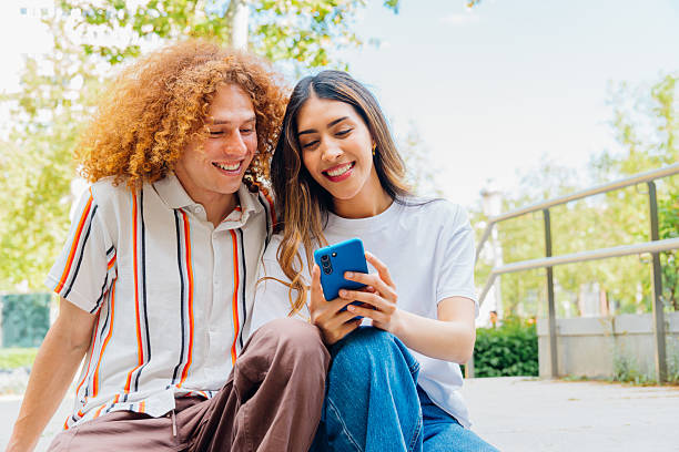 istock Latin couple laughing together, browsing smartphone screen, sitting outdoors during sunny urban day, enjoying intimate moment of connection and joy 2219015259