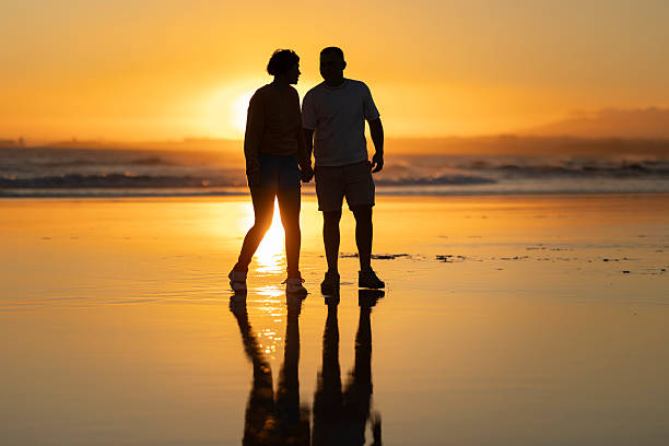 istock Couple holding hands and walking on beach at sunset 2219016788
