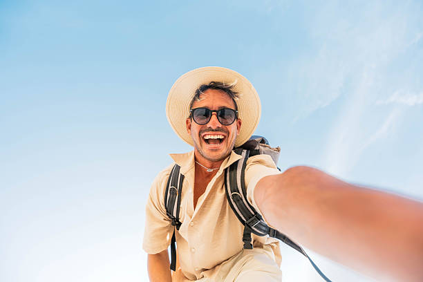 istock Handsome young man taking selfie with smart mobile phone outdoors - Cheerful man smiling at camera on blue sky - Happy tourist enjoying summer vacation - People and technology concept 2219017590
