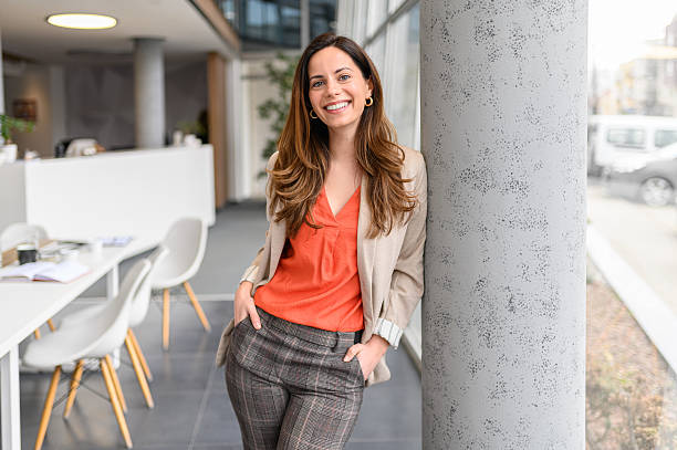 istock Portrait of smiling female manager with hands in pockets posing confidently while standing on column in office 2219019768