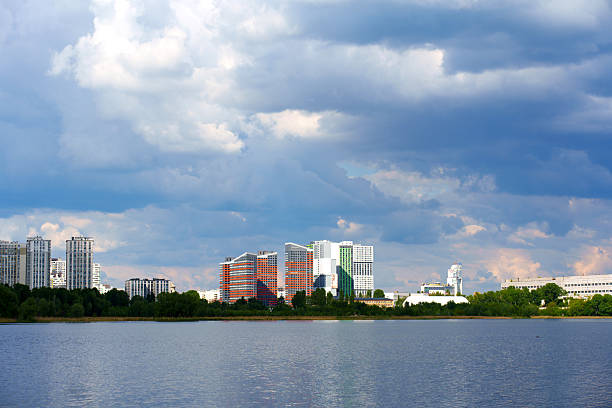 Modern skyline of Putrajaya, Malaysia with tall towers and calm lake under dramatic blue sky and moving white clouds.