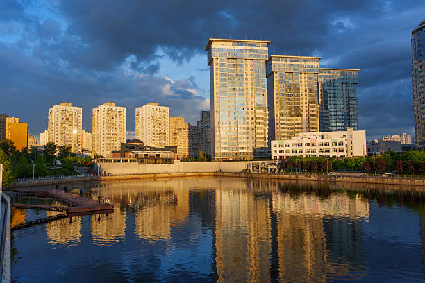 Kyiv, Ukraine - May 19, 2025: Wide-angle shot of modern buildings reflecting on a calm water surface during golden hour in Kyiv, Ukraine.