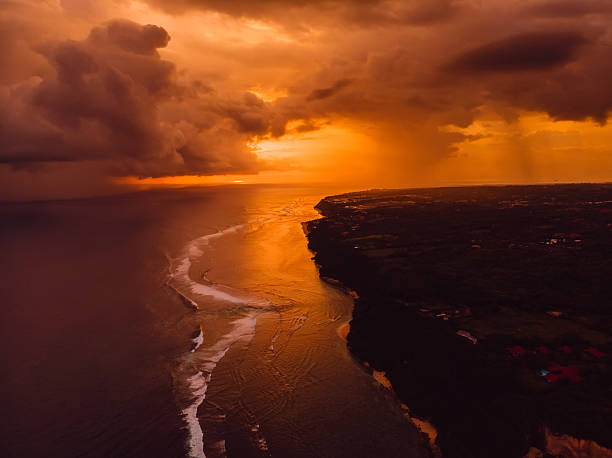 Dramatic coastline at sunset with stormy clouds and golden ocean reflections, aerial tropical landscape view.