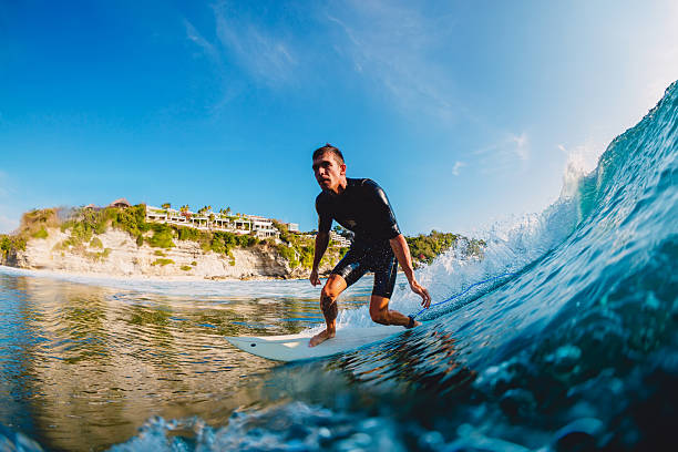 Surfer rides a powerful wave near tropical cliffside beach on a sunny day. Action and adventure lifestyle.