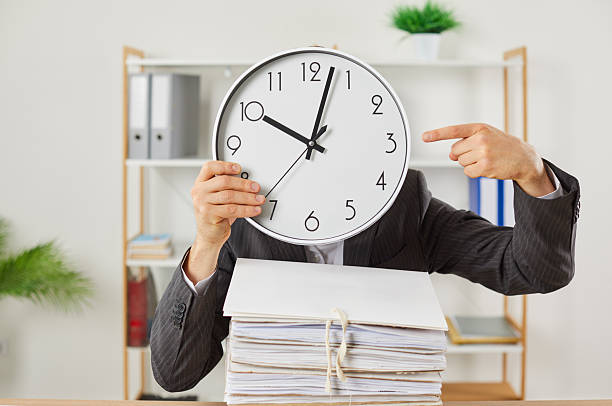 istock Male worker in office, burdened with paper work, points to clock with which he covers his face. 2219028710