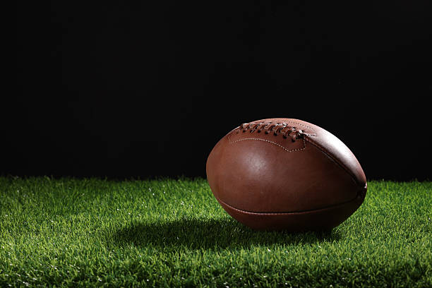 istock A textured American football resting on the green artificial turf with white line. College Football 2219036708
