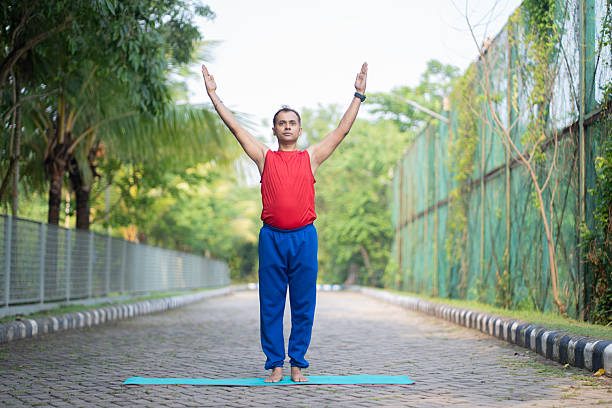 Man performing Urdhva Hastasana (Upward Salute Pose) as part of a yoga routine, standing on a mat in a tranquil outdoor setting.