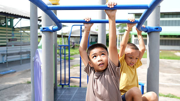 istock Two boys playing colorful playground structure, one hanging from monkey bars with look of concentration, while other sits nearby, enjoying sunny day. Their playful expressions capture joy 2219043967