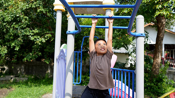 istock Young boy joyfully hangs from playground structure, showcasing his playful spirit and physical strength. vibrant playground setting is surrounded by greenery, creating lively atmosphere 2219043983