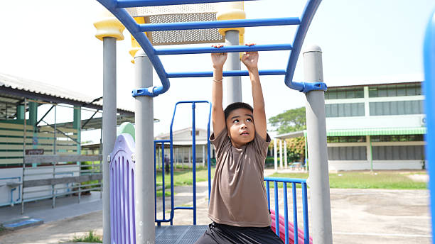 istock Young boy is hanging from playground structure, showcasing his strength and determination. bright, sunny day adds to cheerful atmosphere of playground, making it perfect setting for outdoor play 2219043984