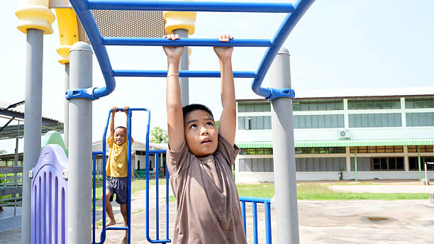 istock Child is hanging from playground structure, showcasing strength and determination, while another child plays in background. scene captures joy of outdoor play and childhood adventure 2219044006