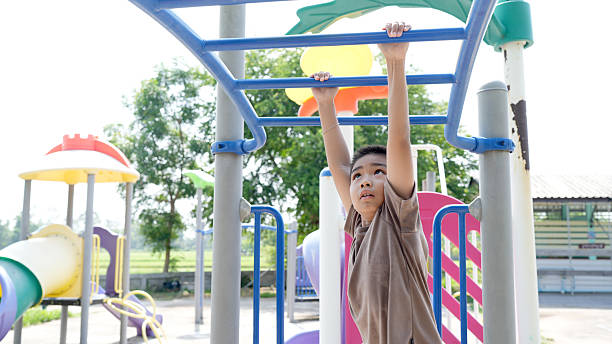 istock Young boy is playing on playground, hanging from monkey bar with focused expression. vibrant play equipment and greenery create lively atmosphere 2219044057