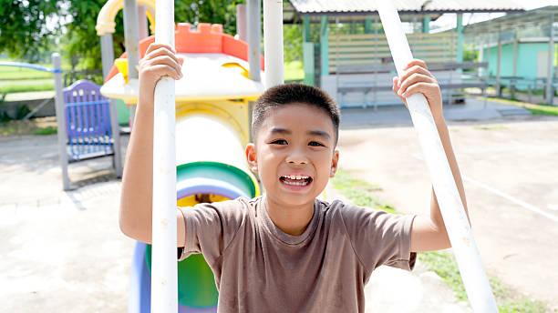 A cheerful boy is playing on colorful playground structure, smiling widely while holding onto bars. bright setting and joyful expression capture essence of childhood fun and adventure