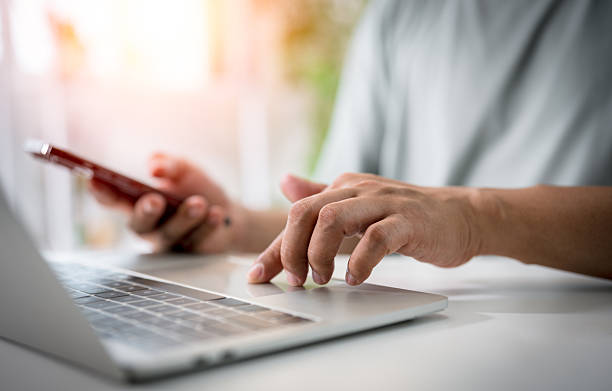 istock Close-up of man hands using laptop computer with mobile phone on office desk. Workspace, businessman working project creative idea for job online network. Business finance and technology concept. 2219045719