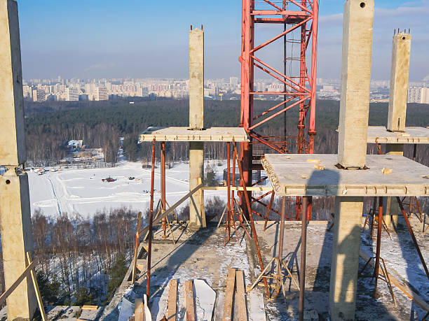 A high-angle shot of a building under construction, with a snowy landscape and cityscape in the background.