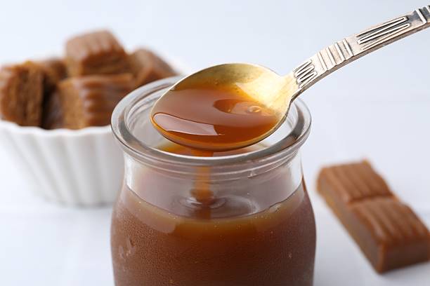 istock Taking tasty caramel sauce from jar with spoon at light table, closeup 2219048982