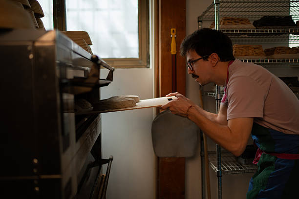 istock Baker taking bread out of oven in bakery 2219050657