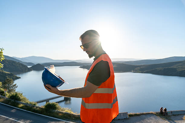 istock Engineer holding helmet observing lake and mountains at sunset 2219052907