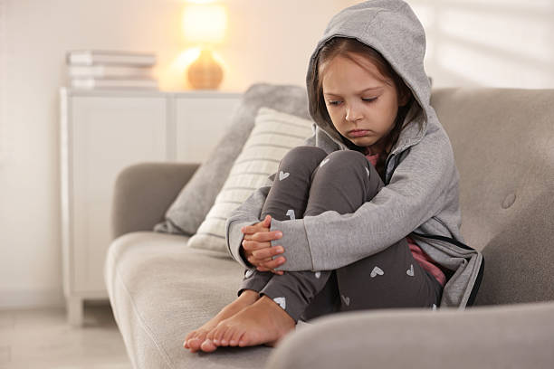 istock Orphanage concept. Sad girl sitting on sofa indoors 2219054873
