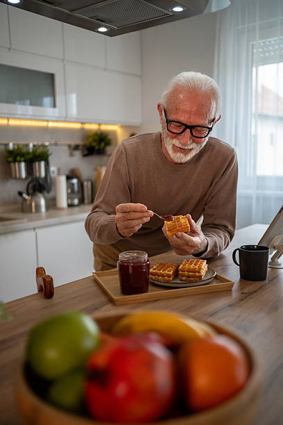 istock Senior man spreading jam on waffles in kitchen 2219054999